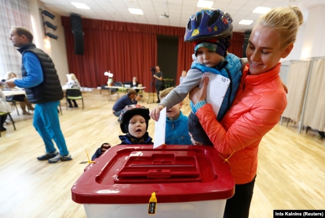 Latvia - A child casts its mother's vote during a general election in Ikskile