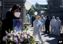 A woman holds a photo of late nurse Marcelino Lopez, who she said died of COVID-10 outside the CNS medical center where he worked in Cochabamba, Bolivia, Thursday, Aug. 6, 2020.