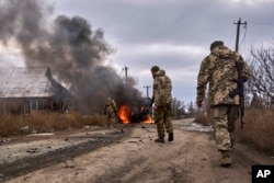 Ukrainian soldiers pass by a volunteer bus burning after a Russian drone hit it near Bakhmut, Donetsk region, on November 23, 2023. (Shandyba Mykyta/Ukrainian 10th Mountain Assault Brigade/via AP)
