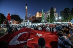 TURKEY -- People, some wearing face masks, wave a giant Turkey national flag and shout slogans outside the Hagia Sophia museum in Istanbul on July 10, 2020.