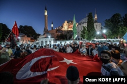 TURKEY -- People, some wearing face masks, wave a giant Turkey national flag and shout slogans outside the Hagia Sophia museum in Istanbul on July 10, 2020.