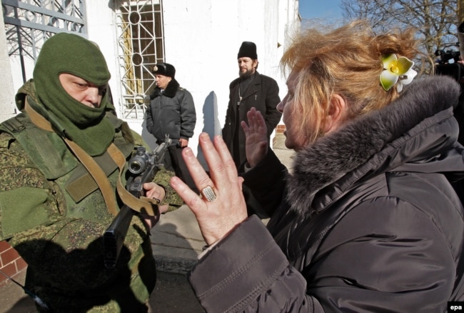 Ukraine -- A Ukrainian woman speaks with an armed man in military uniform, believed to be a Russian soldier blocking the Ukrainian navy base in Novoozerniy village near of Feodosia, Crimea, March 3, 2014