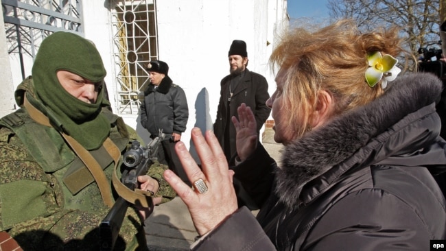 Crimea-- A Ukrainian woman speaks with an armed man in military uniform, believed to be Russian soldiers, block the Ukrainian navy base in Novoozerniy village, March 3, 2014