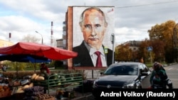 An elderly woman crosses a road in front a mural painting depicting Russian President Vladimir Putin, on the wall of a house, in the town of Kashira, on October 16, 2017. 