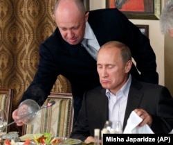 RUSSIA – Evgeny Prigozhin (L) assists then-Russian Prime Minister Vladimir Putin during a dinner with foreign scholars and journalists at the restaurant Cheval Blanc on the premises of an equestrian complex outside Moscow, November 11, 2011.