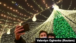 UKRAINE -- A couple wearing protective masks against COVID-19 take a selfie in a front of Christmas tree in central Kyiv, Ukraine December 20, 2020. 