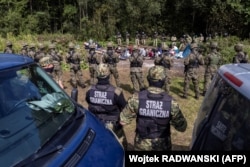 Polish border guards stand next to migrants believed to be from Afghanistan in the small village of Usnarz Gorny near Bialystok, northeastern Poland, located close to the border with Belarus, on August 20, 2021. (AFP)