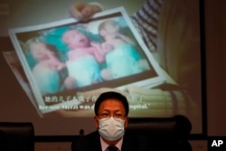 Xu Guixiang, a deputy spokesperson for the Xinjiang regional government, looks up near a slide showing a photo of Uighur infants during a press conference to refute accusations of genocide in Beijing, China on January 10, 2010. (AP Photo/Ng Han Guan)