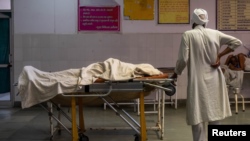 A man stands next to the body of his wife, who died due to breathing difficulties, inside an emergency ward of a government hospital in Bijnor, Uttar Pradesh, India, May 11, 2021. 