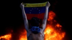 CARACAS – A protester holds a national flag as a bank branch, housed in the magistracy of the Supreme Court of Justice, burns during a rally against Venezuela's President Nicolas Maduro, in Caracas, Venezuela, June 12, 2017.