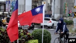 This photo taken on December 22, 2023 shows a cyclist next to two Taiwanese national flags in Taipei.