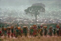 In this May 17, 1994 photo, refugees who fled the ethnic bloodbath in Rwanda carry water containers back to their huts at the Benaco refugee camp in Tanzania, near the border with Rwanda.