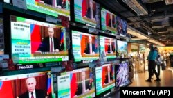 People stand by TV screens broadcasting the news of Russian invasion of Ukraine, in Hong Kong, Feb. 24, 2022. (AP/Vincent Yu)