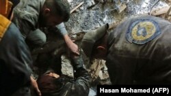 SYRIA -- Volunteers of the Syrian Civil Defense, known as the White Helmets, rescue a woman from the rubble of a building after an air strike in Douma, Eastern Ghouta, March 19, 2018