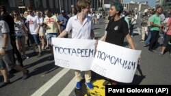 Protesters stand on a portrait of Russian President Vladimir Putin during an opposition rally in Moscow, Russia, Sunday, July 29, 2018. Banners read from left: "Get old", "Be quiet". 