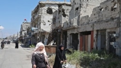 Syrians walk past buildings heavily damaged during Syria's civil war, in the central city of Homs, on April 28, 2020.