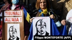 Women hold placards reading "International Criminal Court in The Hague" above the portraits of both Russian President Vladimir Putin and Belarusian leader Alexander Lukashenko during a demonstration in support of Ukraine in Rome on February 24, 2022. (Filippo Monteforte/AFP)