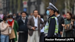 A police officer wearing a face mask monitors pedestrian traffic along a street in Shanghai on October 28, 2020. (Photo by Hector Retamal / AFP)