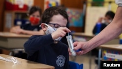 A child places his testing swab in the vial for pool testing to prevent the spread of the coronavirus disease (COVID-19) in the classroom at South Boston Catholic Academy in Boston, Massachusetts, U.S., January 28, 2021. REUTERS/Allison Dinner