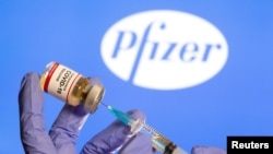  A woman holds a small bottle labeled with a "Coronavirus COVID-19 Vaccine" sticker and a medical syringe in front of Pfizer logo on October 30, 2020. (Dado Ruvic/Reuters)