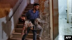 Syria -- A Syrian man carries a severely wounded boy at a make-shift hospital in the rebel-held town of Douma, east of the capital Damascus, following reported cluster bomb shelling, October 20, 2016