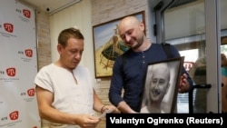 UKRAINE -- Russian dissident journalist Arkady Babchenko (R) holds his portrait while listening to deputy chief of the Crimean Tatar channel ATR Aider Muzhdabayev at the office of the channel in Kyiv, May 31, 2018