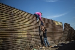 A group of Central American migrants climb the border fence between Mexico and the United States, near El Chaparral border crossing, in Tijuana, Baja California.