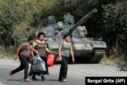 GEORGIA -- Georgian refugees are seen walking past a Russian armoured vehicle in the village of Igoeti, 50 kilometers (31 miles) from Tbilisi, August 16, 2008