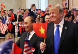 Former U.S. President Donald Trump and then Vietnamese Prime Minister Nguyen Xuan Phuc hold flags as they are greeted by students during their meeting at the Office of Government Hall in Hanoi, on Feb 27, 2019.