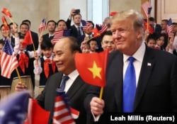 Former U.S. President Donald Trump and then Vietnamese Prime Minister Nguyen Xuan Phuc hold flags as they are greeted by students during their meeting at the Office of Government Hall in Hanoi, on Feb 27, 2019.