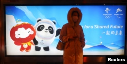 A woman waits on a bus station in front of an advertising board featuring Bing Dwen Dwen, the Beijing 2022 Winter Olympic Mascot and Shuey Rhon Rhon, the 2022 Beijing Winter Paralympic Games Mascot, in Beijing on January 19, 2022. (Fabrizio Bensch/Reuters)