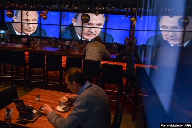 RUSSIA -- A man drinks a coffee in front of screens broadcasting Russian President Vladimir Putin's annual press conference, at a bar in Moscow, December 20, 2018.