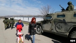 Ukraine -- Women walk along a road passing a Russian 'GAZ Tigr' infantry mobility vehicle outside the territory of a Ukrainian military unit in the village of Perevalnoye, outside Simferopol, Ukraine, 14 March 2014