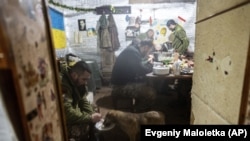 A Ukrainian serviceman feeds his dog as other soldiers eat in a shelter at the frontline positions near Zolote in the Luhansk region, February 7, 2022.(Evgeniy Maloletka/AP)
