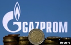 Euro coins are seen in front of displayed logo of Gazprom
