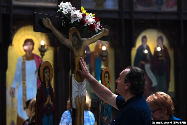 NORTH MACEDONIA -- A man touches the wooden statue of Jesus Christ on a cross at the main Orthodox church St. Kliment in Skopje on Good Friday, April 26, 2019