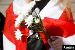 A woman holding flowers and wrapped in the historical white-red-white flag of Belarus attends an action in support of the Belarusian opposition in Warsaw, Poland on September 9, 2020.