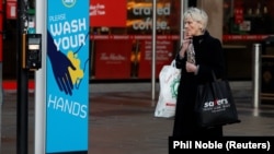 A woman smokes a cigarette as she stands by a sign encouraging people to wash their hands amid the outbreak of the coronavirus disease (COVID-19) in Belfast, Northern Ireland January 2, 2021.