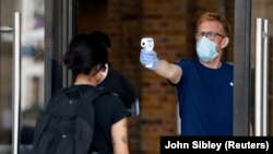 A staff member tests another member's temperature at the Apple store in Covent Garden before its reopening, following the outbreak of the coronavirus disease (COVID-19) in London, Britain June 15, 2020. 