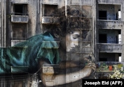 LEBANON -- Graffiti of a boy working on an electronic device is seen on a building riddled with holes from shrapnel dating back from the Lebanese civil war (1975-1990) in Beirut on Sep 26, 2017 AFP JOSEPH EID