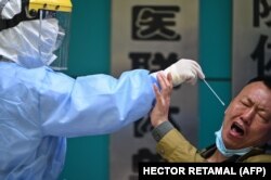 A man being tested for the COVID-19 novel coronavirus reacts as a medical worker takes a swab sample in Wuhan in China's central Hubei province on April 16, 2020.