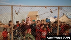 Displaced Syrian children stand behind a fence outside their tents a camp set up in Idlib's northern countryside near the Syria-Turkey border, October 22, 2019. (Aaref Watad/AFP)