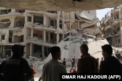 SYRIA -- People watch as members of the Syrian Civil Defence, also known as the "White Helmets", search the rubble of a collapsed building following an explosion in the town of Jisr al-Shughur, in the west of the mostly rebel-held Syrian province of Idlib