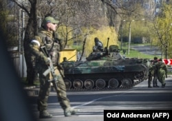 Russian-led forces stand next to a vehicle as they close off a road in Donetsk