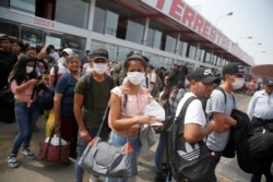 Peru - People wearing face masks wait to board a bus at a bus station after Peru's government deployed military personnel to block major roads, as the country rolled out a 15-day state of emergency to slow the spread of coronavirus disease (COVID-19).