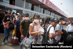 Peru - People wearing face masks wait to board a bus at a bus station after Peru's government deployed military personnel to block major roads, as the country rolled out a 15-day state of emergency to slow the spread of coronavirus disease (COVID-19).