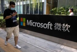A man looks at his smartphone as he walks by the Microsoft office in Beijing on August 7, 2020. (AP)