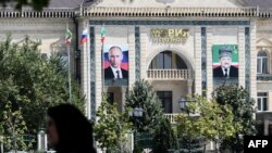 A woman walks on an avenue named after Russian President Vladimir Putin in front of the Grozny city administration's building displaying portraits of Russian President Vladimir Putin (L) and Akhmad Kadyrov (R), former Chechen Republic's president / AFP Photo