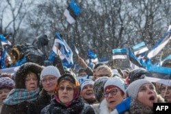 People wave Estonian flags in front of the Estonian Parliament during a festive ceremony to celebrate 100 years since Estonia declared independence for the first time in 1918, in Tallinn on February 24, 2018. / AFP PHOTO / Raigo Pajula