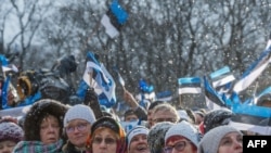 People wave Estonian flags in front of the Estonian Parliament during a festive ceremony to celebrate 100 years since Estonia declared independence for the first time in 1918, in Tallinn on February 24, 2018. / AFP PHOTO / Raigo Pajula